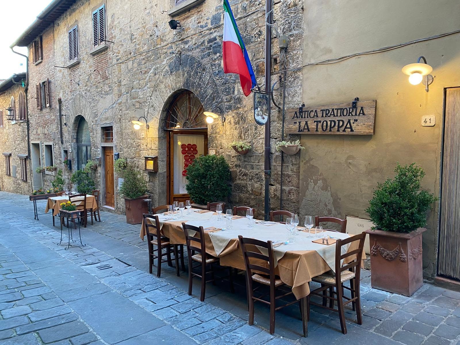 Antica Trattoria La Toppa in San Donato in Poggio: tables laid on the stone-paved street outside the old stone façade, under the trattoria’s wooden sign