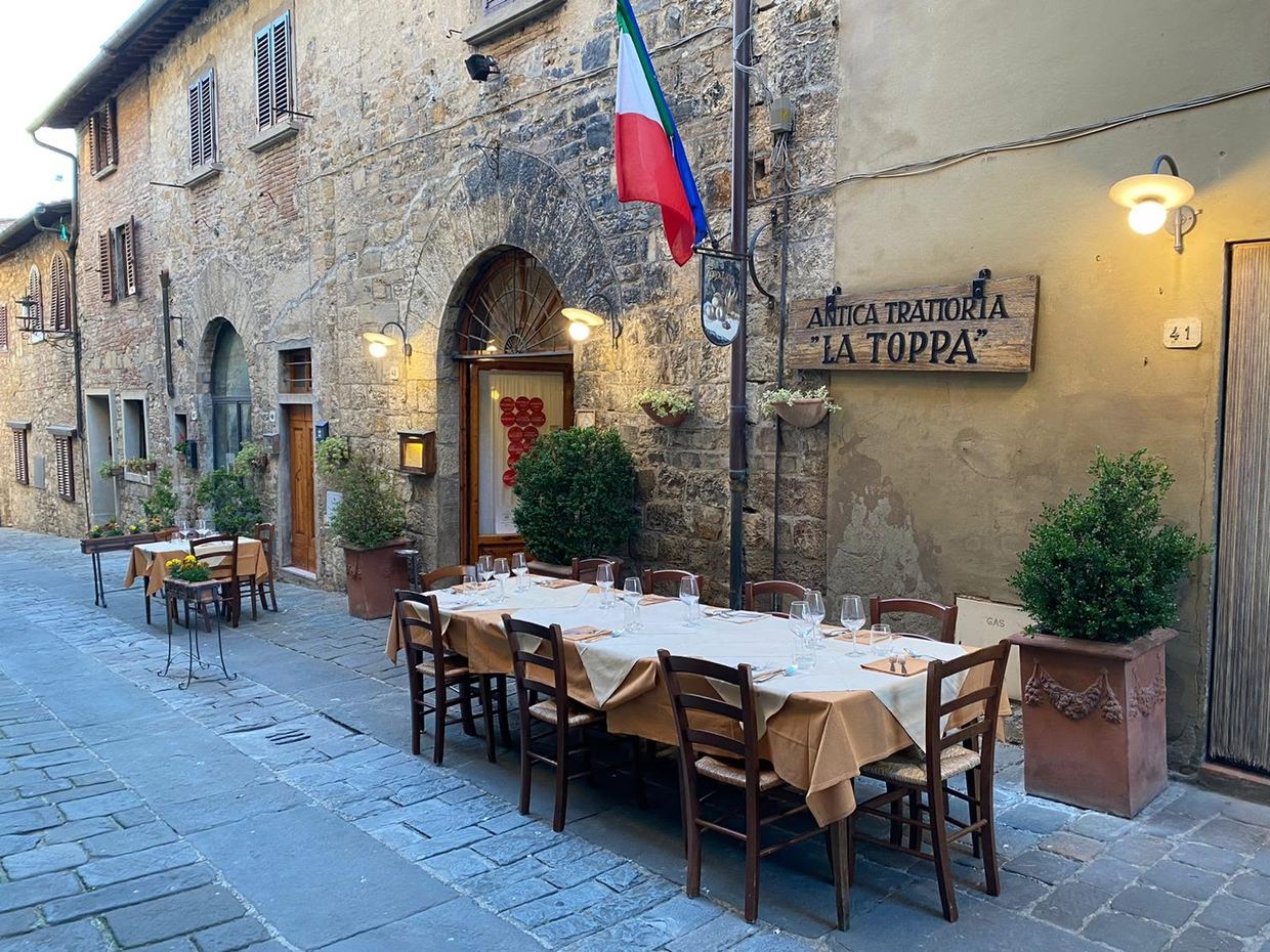 Antica Trattoria La Toppa in San Donato in Poggio: tables laid on the stone-paved street outside the old stone façade, under the trattoria’s wooden sign