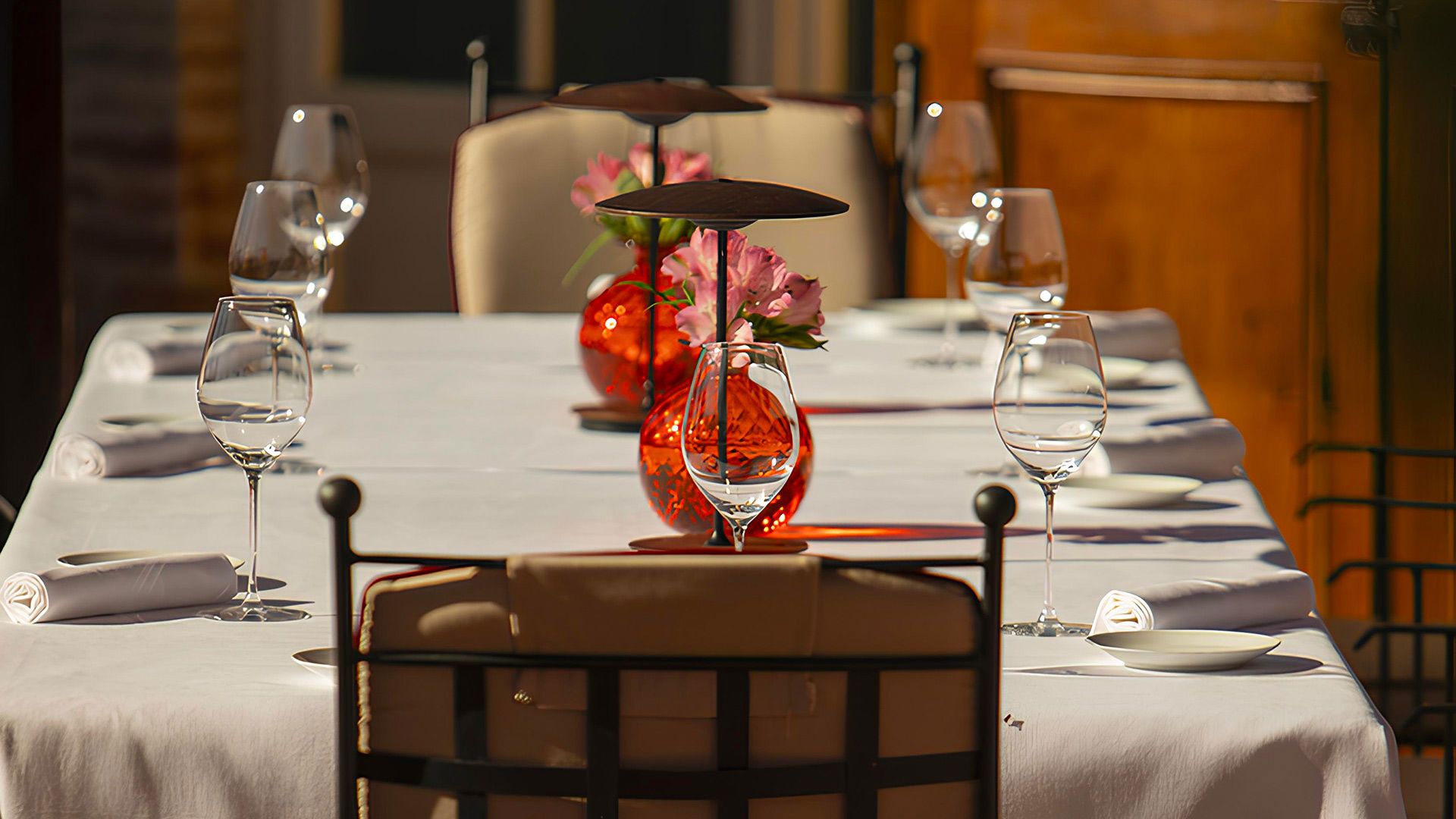 A table laid for dinner at Poggio Rosso, Borgo San Felice: white linen, wine glasses and red glass vases with pink flowers in the evening light