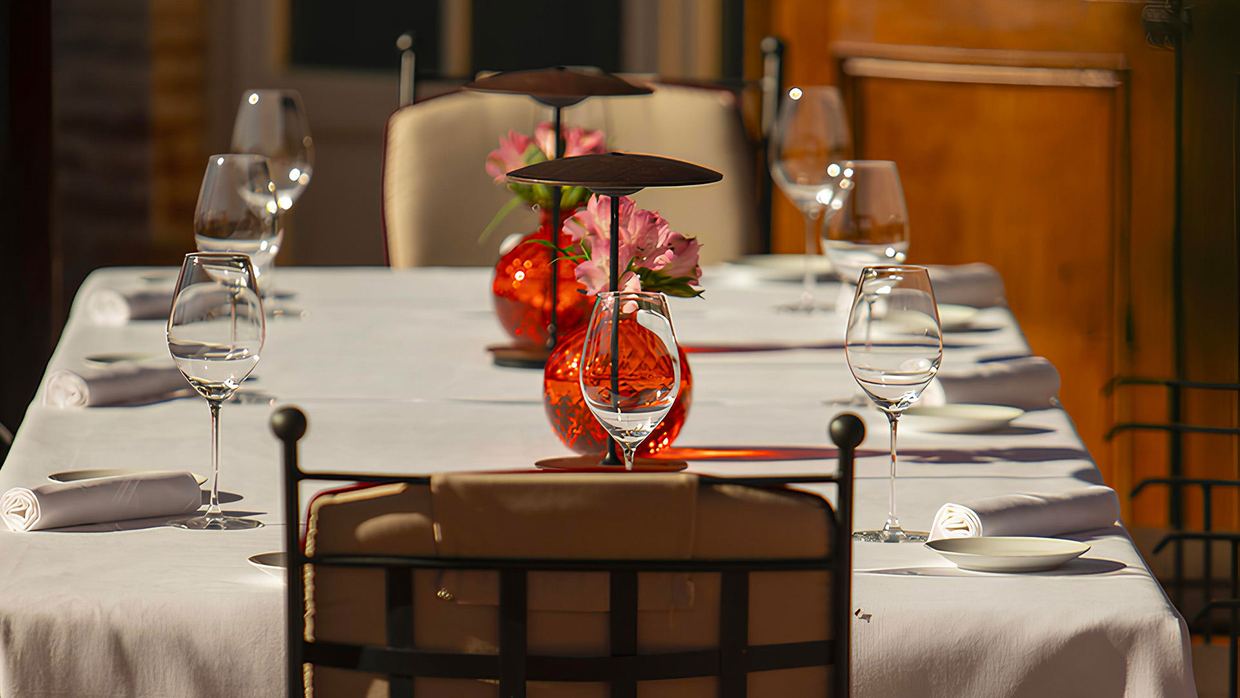A table laid for dinner at Poggio Rosso, Borgo San Felice: white linen, wine glasses and red glass vases with pink flowers in the evening light