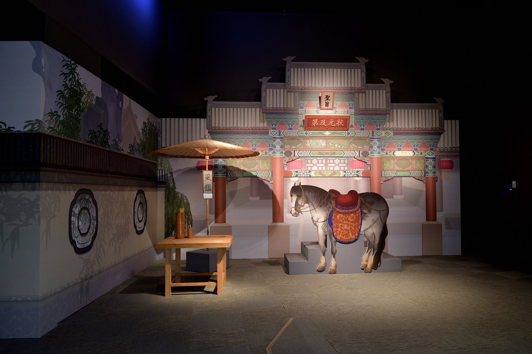 重現畫中街景的牌樓、馬匹與傘桌場景。/ A recreated street scene from the painting with an archway, horse and parasol table.