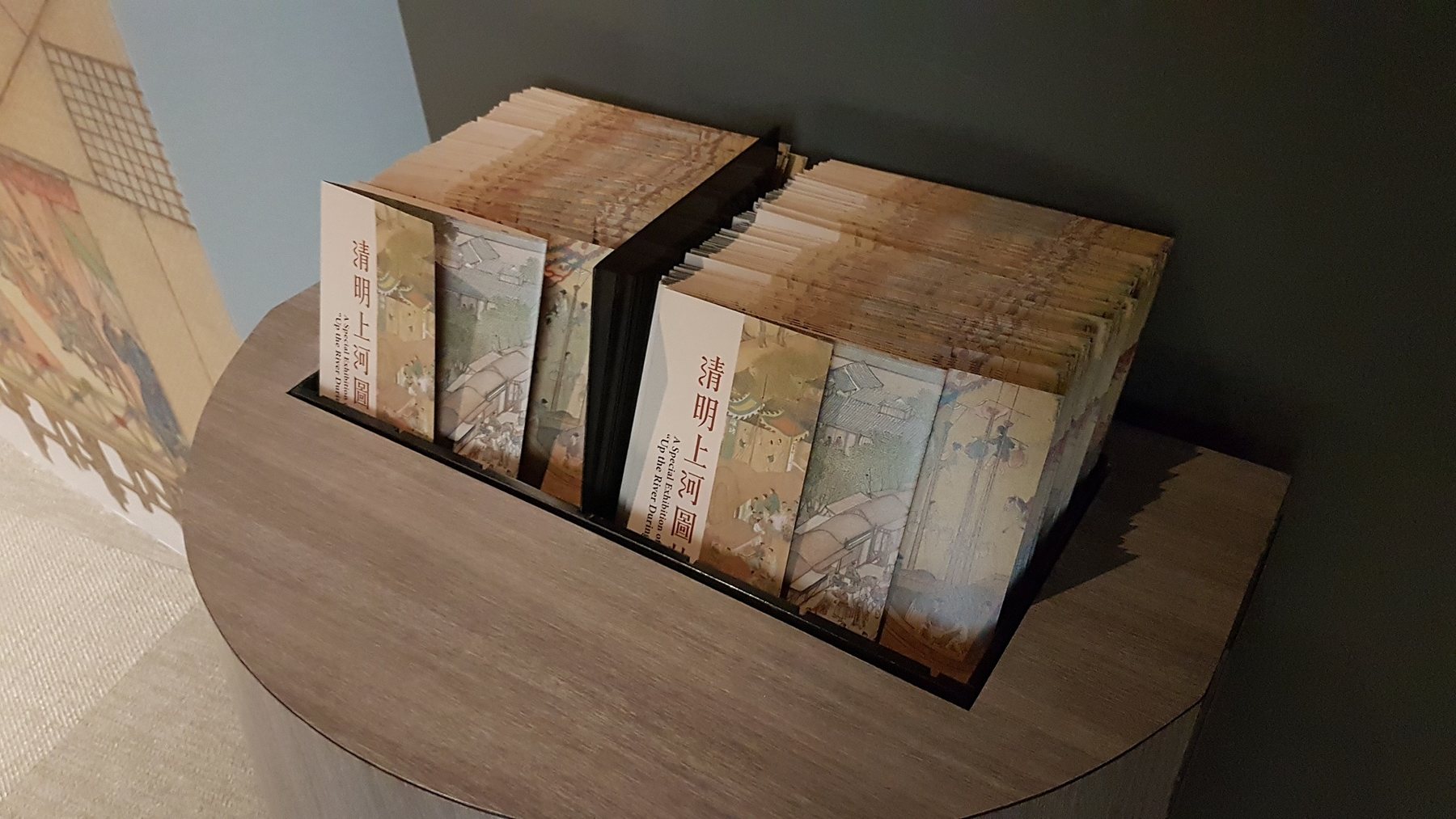 展台上陳列的《清明上河圖特展》摺頁。/ Exhibition brochures displayed on a round stand.