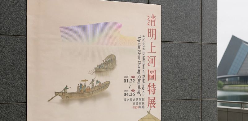 故宮南院建築旁牆面張貼《清明上河圖特展》主視覺海報,霧橘底色與舟船剪影。/ The Up the River During Qingming key visual poster mounted on a wall beside the NPM Southern Branch building.