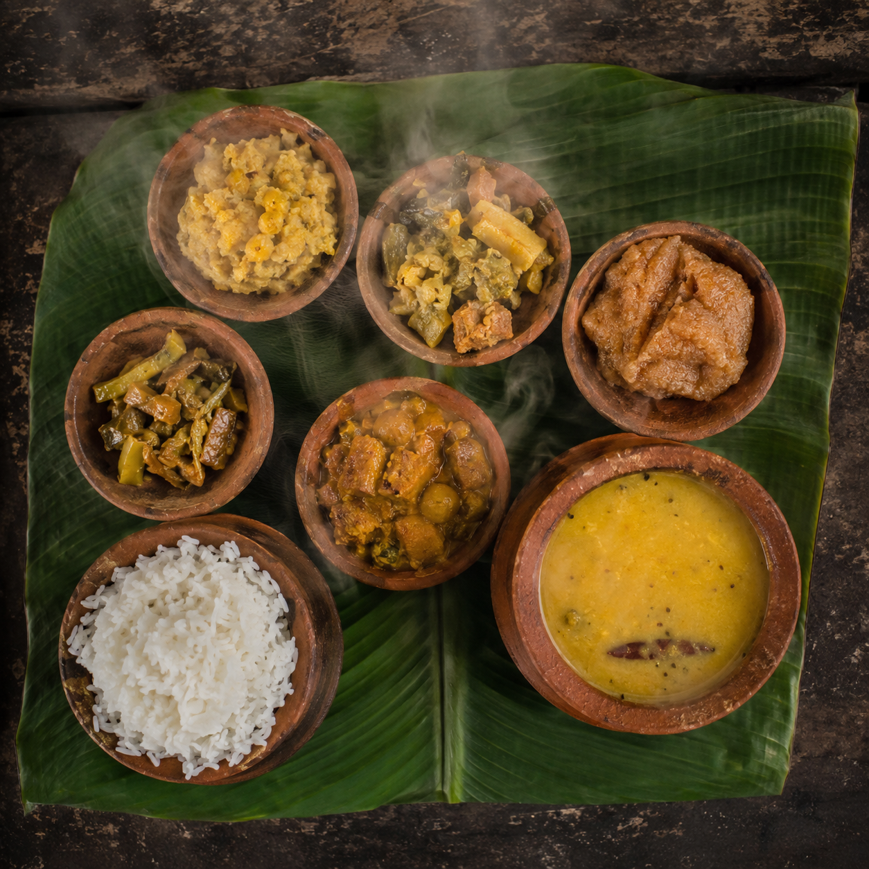 Mahaprasad served in small earthen pots on a banana leaf — rice, dalma, curries and a sweet