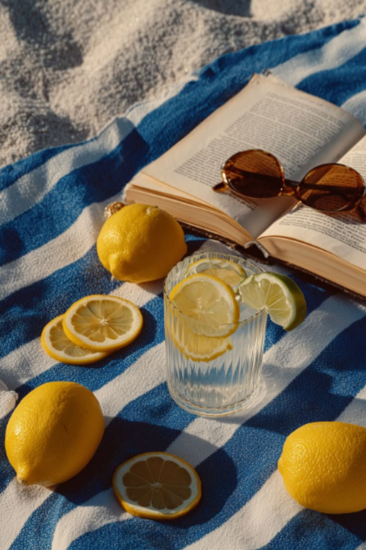 Open book, sunglasses, citrus and a drink on a blue striped towel