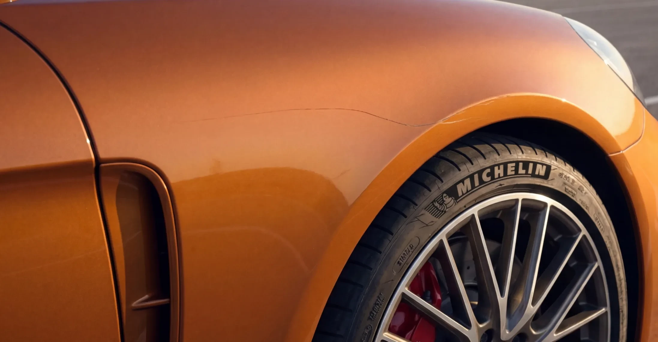 Scratch along the front fender of an orange sedan