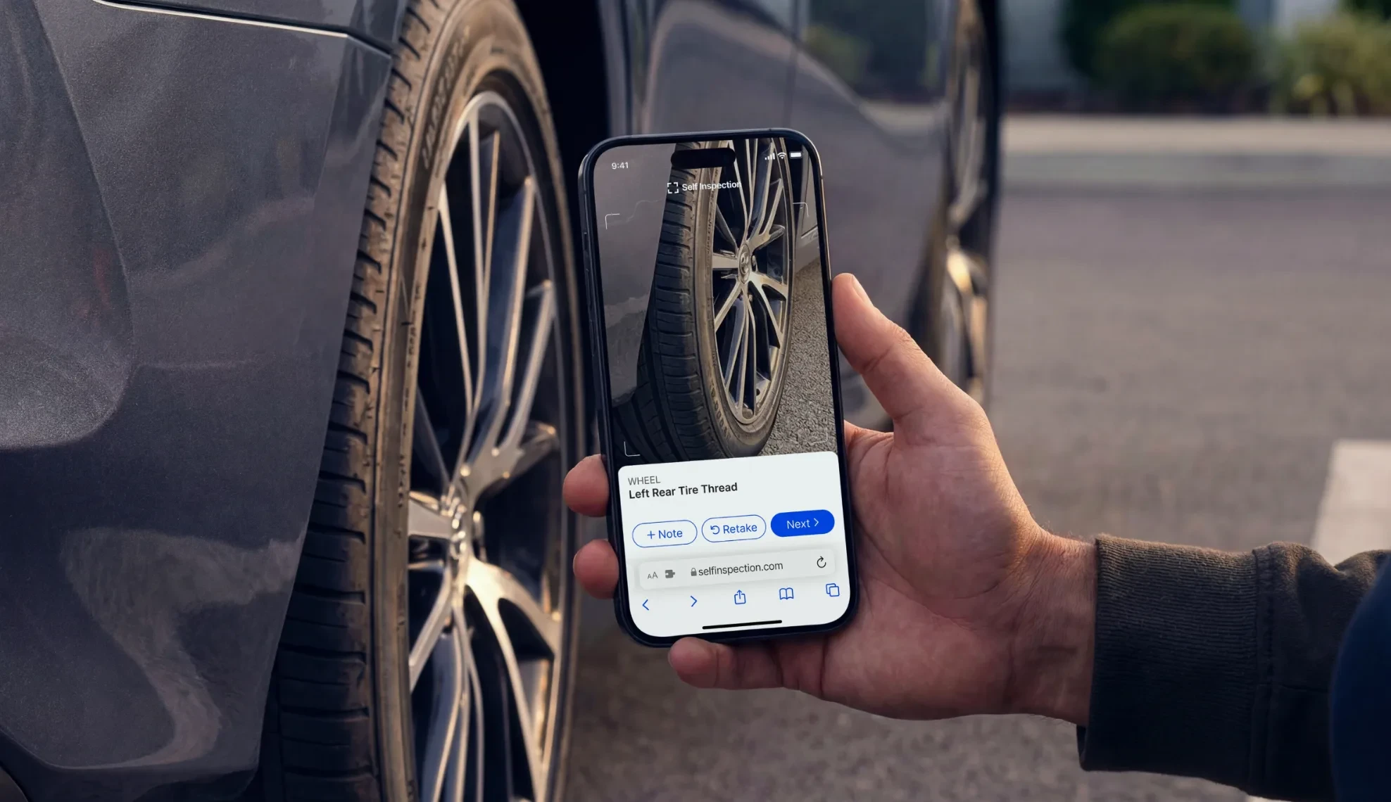 Hand holding a phone capturing the left rear tire tread in a browser