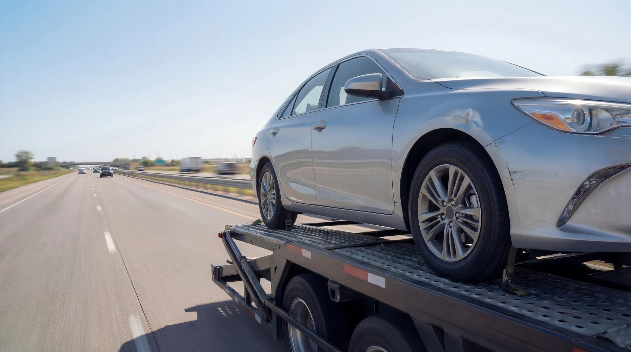 Silver sedan with front-end damage loaded on a car carrier trailer, on the highway