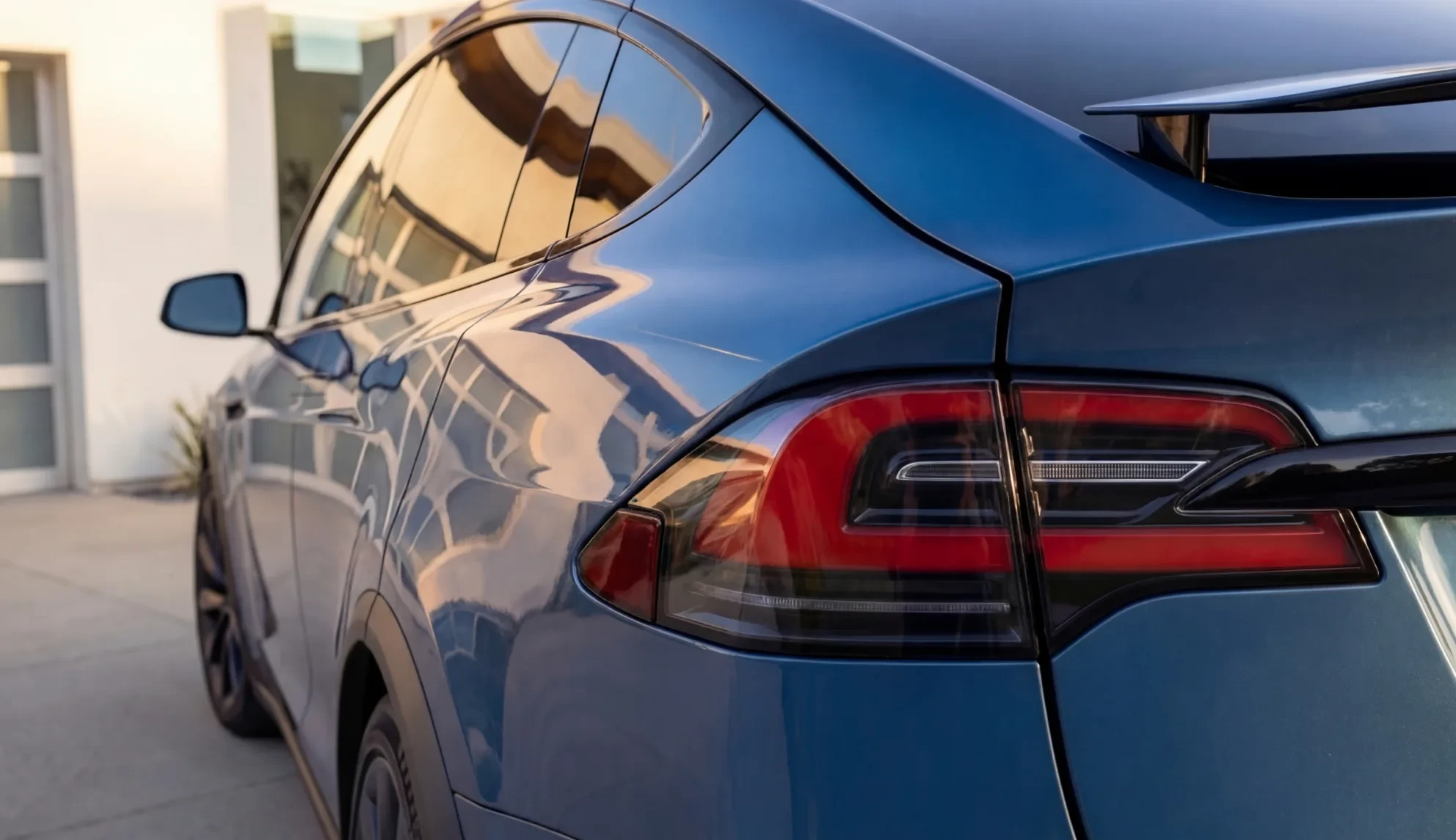 Rear quarter panel and tail light of a blue Tesla Model X parked in a driveway