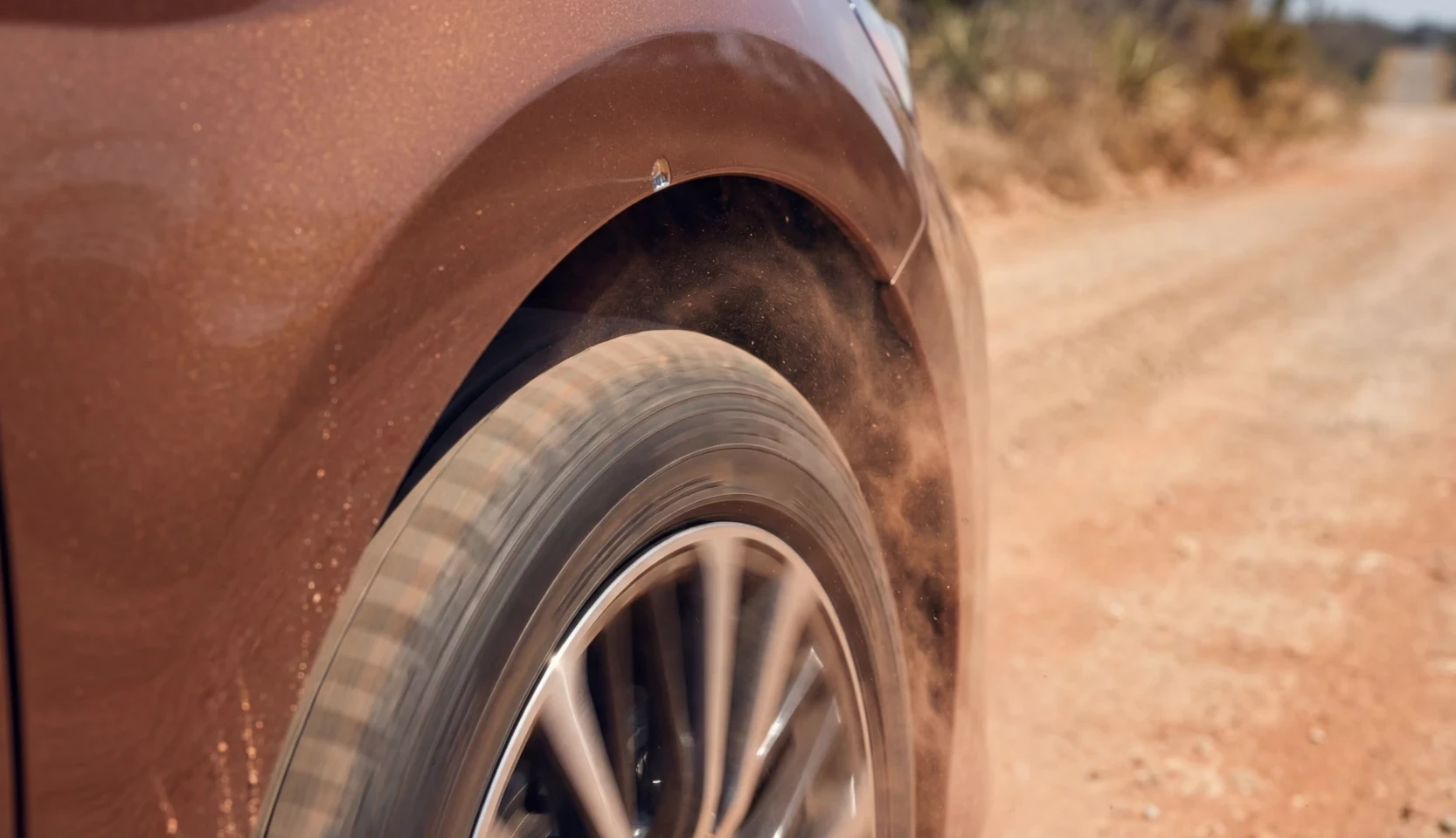 Front tire and wheel arch of a copper SUV kicking up dust on a dirt road
