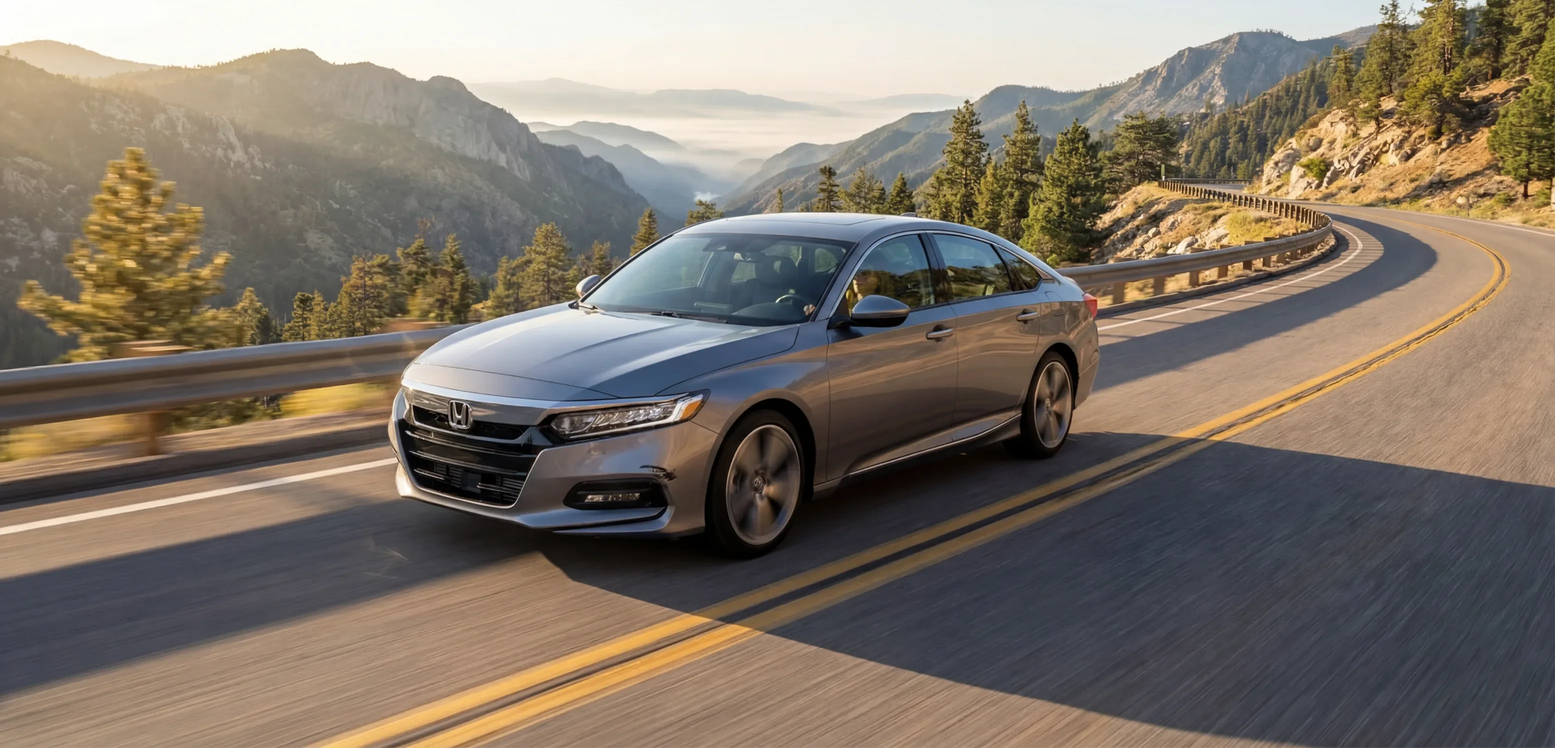 Silver sedan driving a mountain road at sunrise
