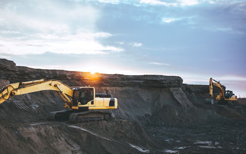 Two machines digging in a mine when the sun is rising