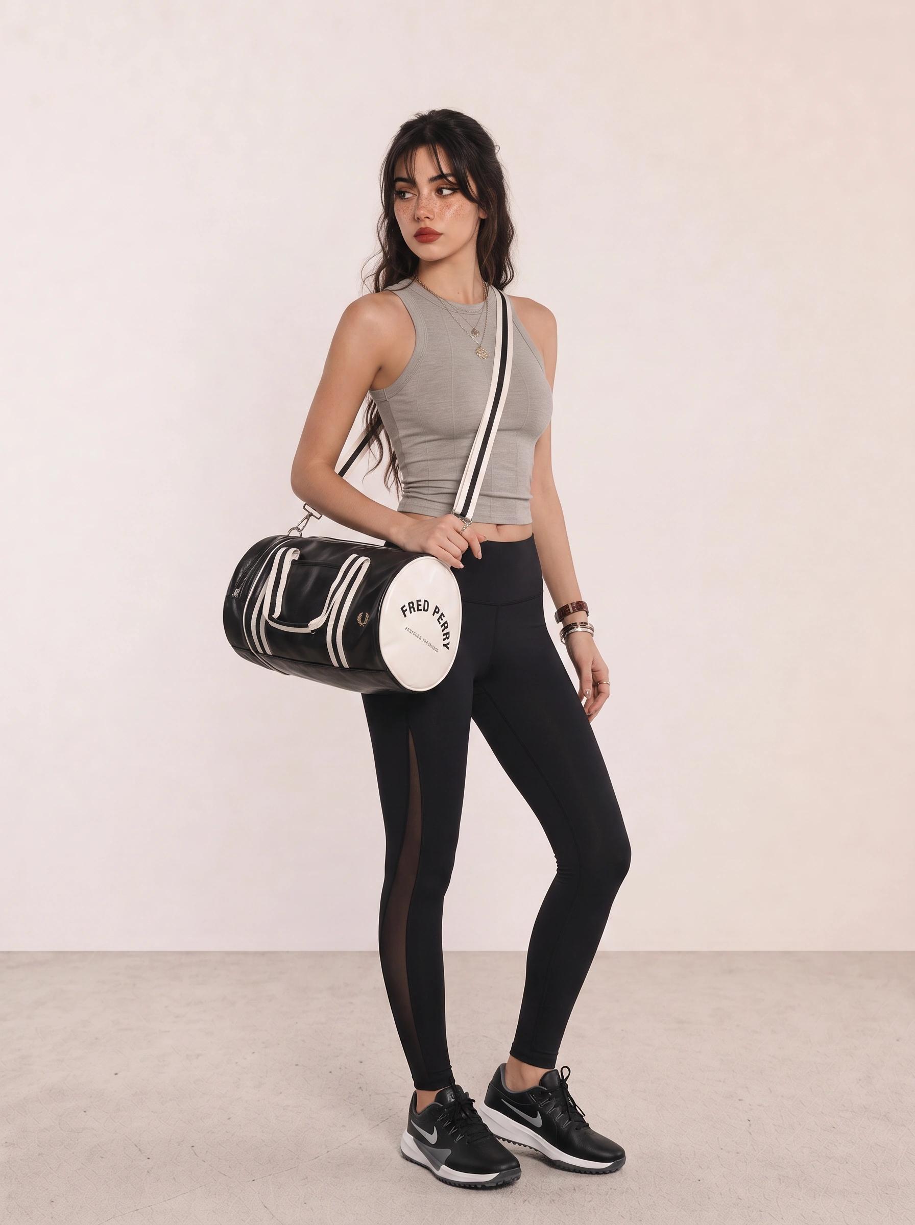 Woman wearing a grey crop tank, black leggings, black running shoes, and a black duffel bag