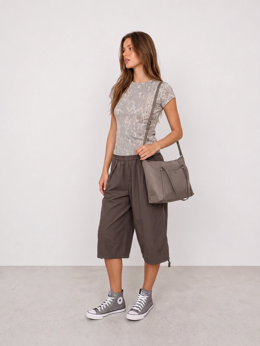 Frau trägt ein Animal-Print-Shirt, anthrazitfarbene Bermudashorts, graue High-Top-Sneaker und eine graue Schultertasche
