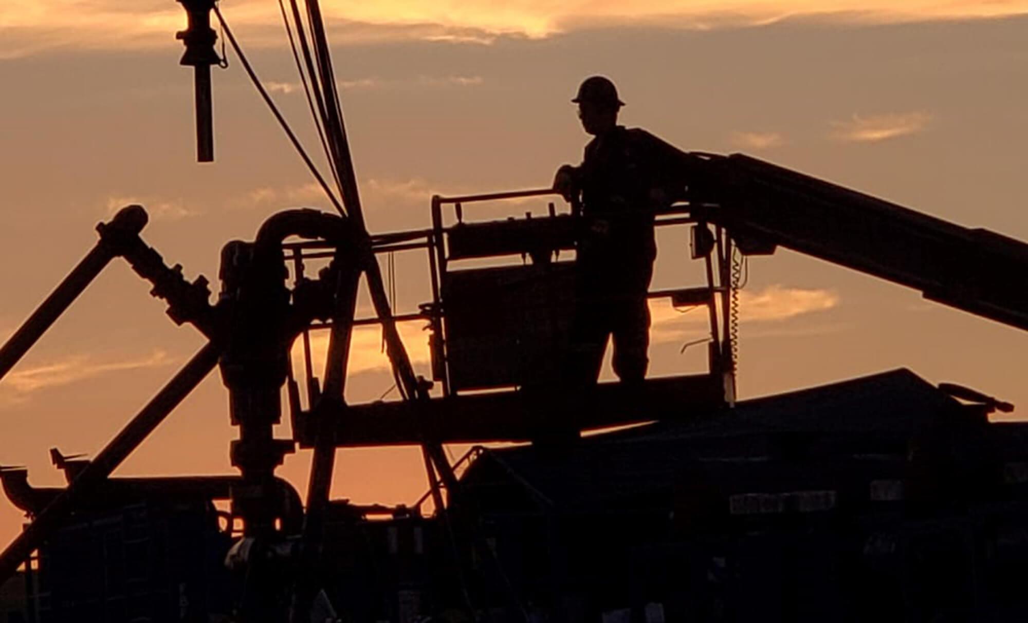 Man on Heavy Equipment Silhouetted against Sunset