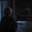 Person alone at a kitchen table at night after noticing signs of an emotional affair, phone face down beside them.