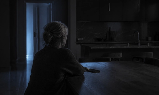 Person alone at a kitchen table at night after noticing signs of an emotional affair, phone face down beside them.