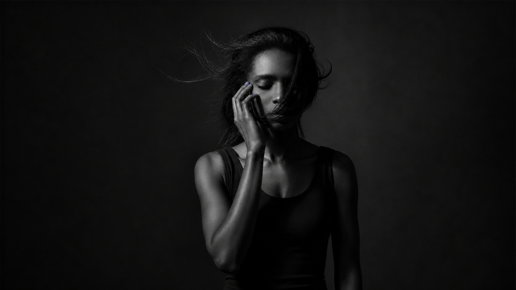 A woman alone in dim light with her eyes closed, sitting with the question of whether infidelity is a dealbreaker.