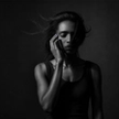 A woman alone in dim light with her eyes closed, sitting with the question of whether infidelity is a dealbreaker.