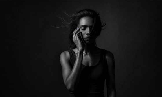 A woman alone in dim light with her eyes closed, sitting with the question of whether infidelity is a dealbreaker.