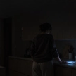 Woman awake alone in a dark kitchen with a phone glowing on the counter, illustrating the checking pattern described in relationship OCD.
