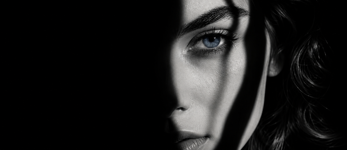 Woman's face half in shadow with a single tear, capturing the isolation of betrayal trauma