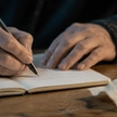 Hands writing in a private journal, one page torn and rewritten, forgiving yourself for cheating