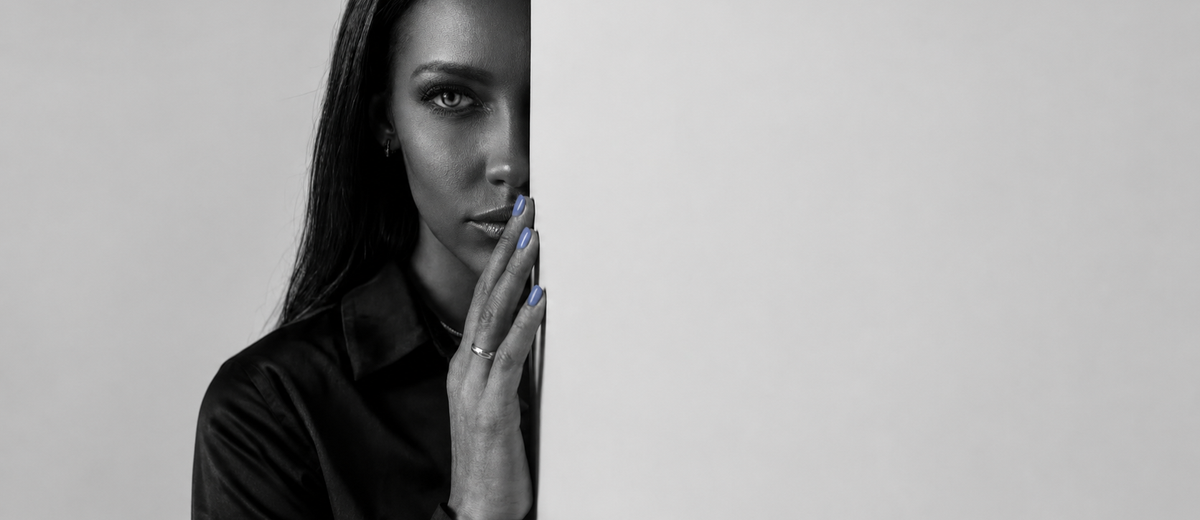 Woman half-hidden behind a wall weighing reconciliation after infidelity, hand raised to her lips.