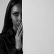Woman half-hidden behind a wall weighing reconciliation after infidelity, hand raised to her lips.