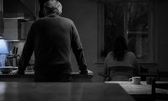 Older man and younger woman apart in a dim kitchen at night, illustrating the distance in age gap relationships