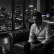 Should I confess to my infidelity: a man sits alone at night in a dark study, hands clasped, weighing the decision.