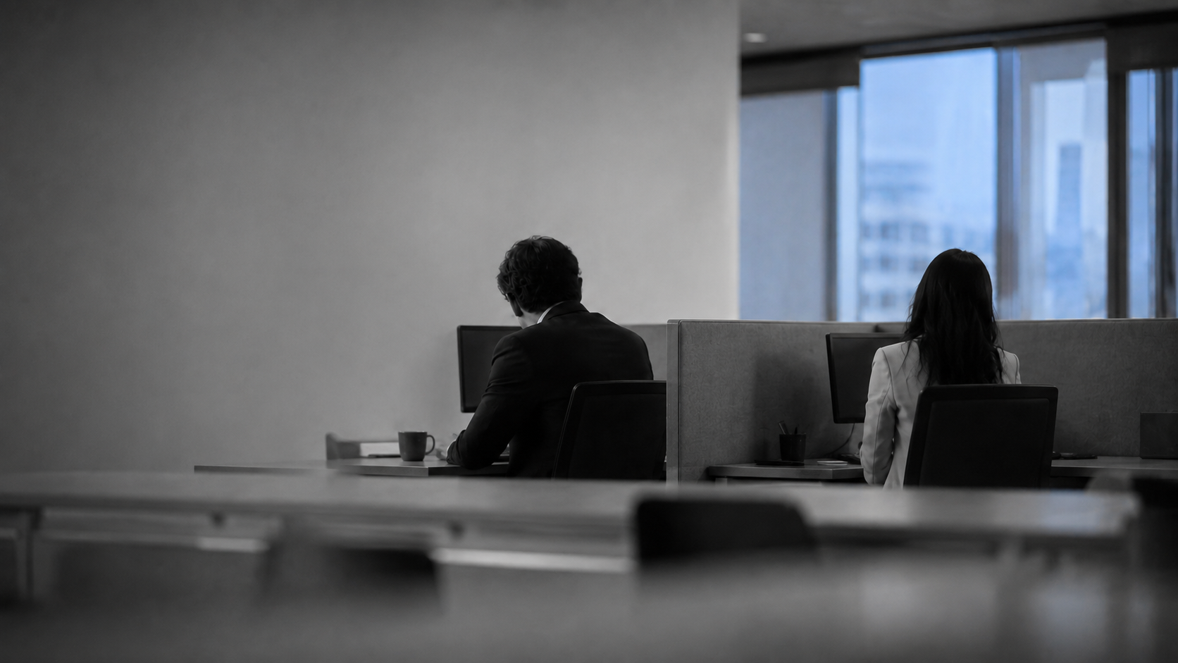 Two coworkers seated at opposite ends of a office table, backs to camera, showing the distance of a workplace affair