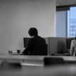 Two coworkers seated at opposite ends of a office table, backs to camera, showing the distance of a workplace affair