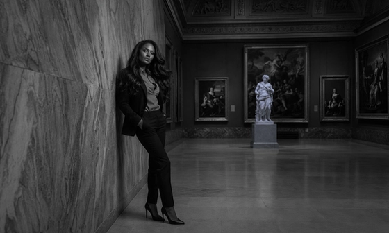 Woman standing alone and reflective in a quiet gallery, illustrating obsessive thoughts after betrayal. Black and white portrait.