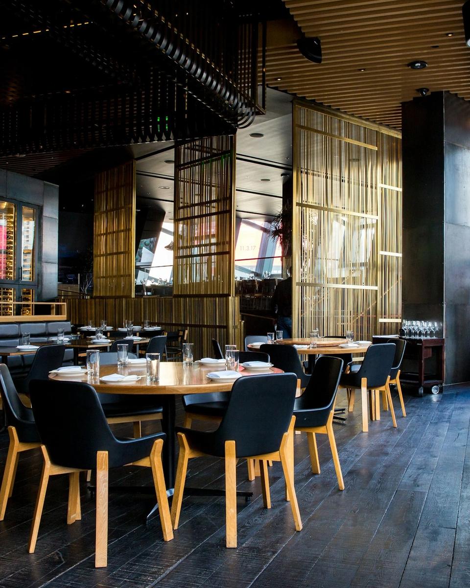 Salle du restaurant aux tables en bois et chaises noires sous un éclairage chaleureux