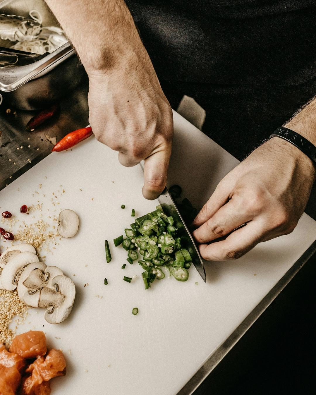 Mains du cuisinier taillant des légumes frais au couteau sur une planche