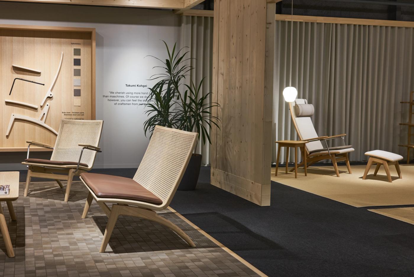 GAZE lounge chairs in oak with woven rattan backs and brown leather seats in the foreground, with a GAZE high-back chair and footstool in the background beside a wooden partition and a plant.
