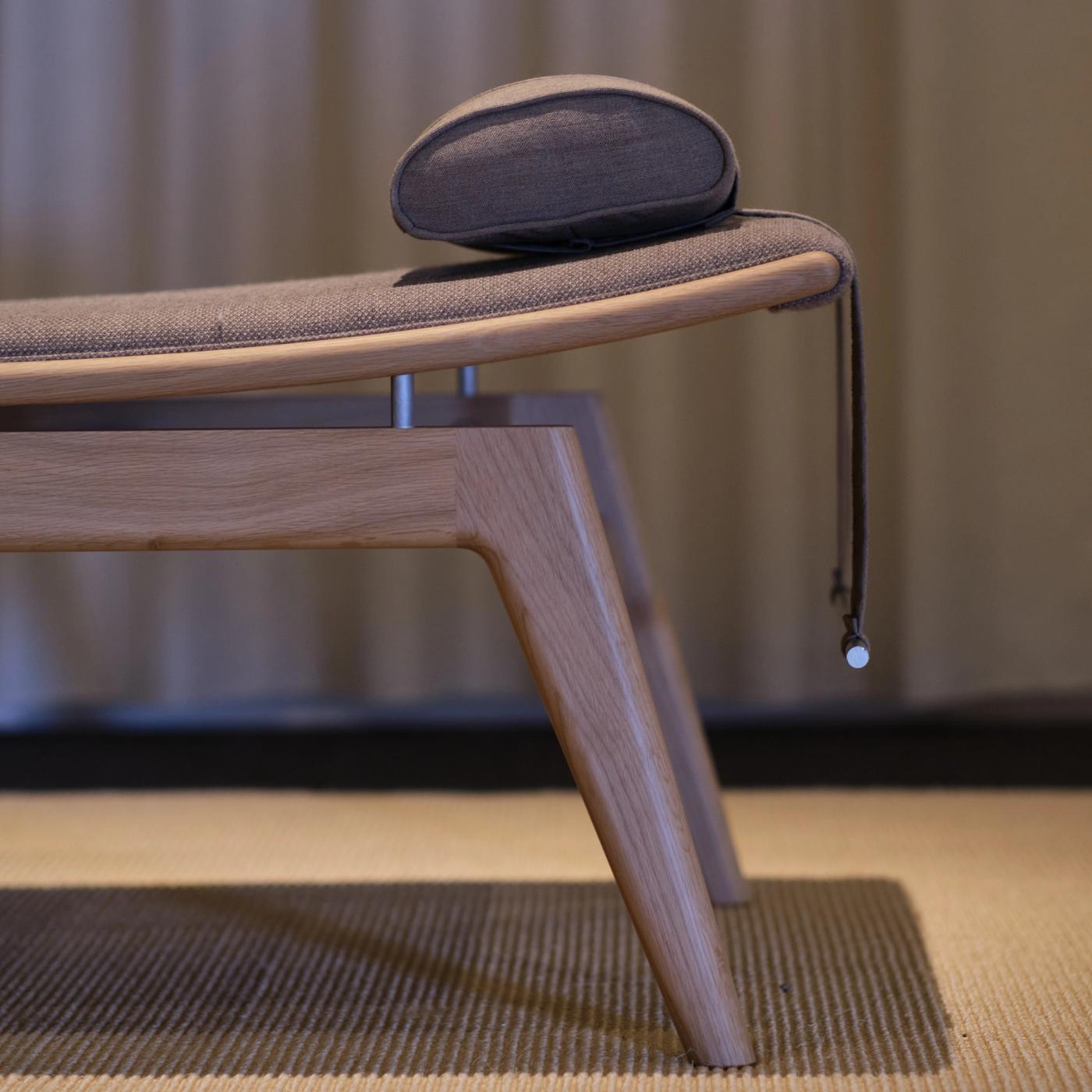 Alt-tekst:  Close-up of a GAZE daybed with an oak frame, an upholstered seat and a neck cushion with a leather strap, on a textured rug.