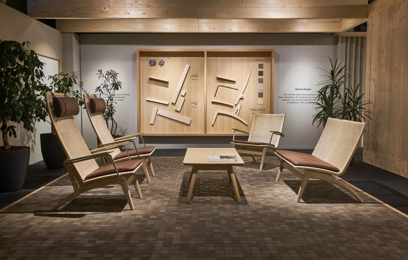 around a low oak table in an exhibition space with a wooden wall display.