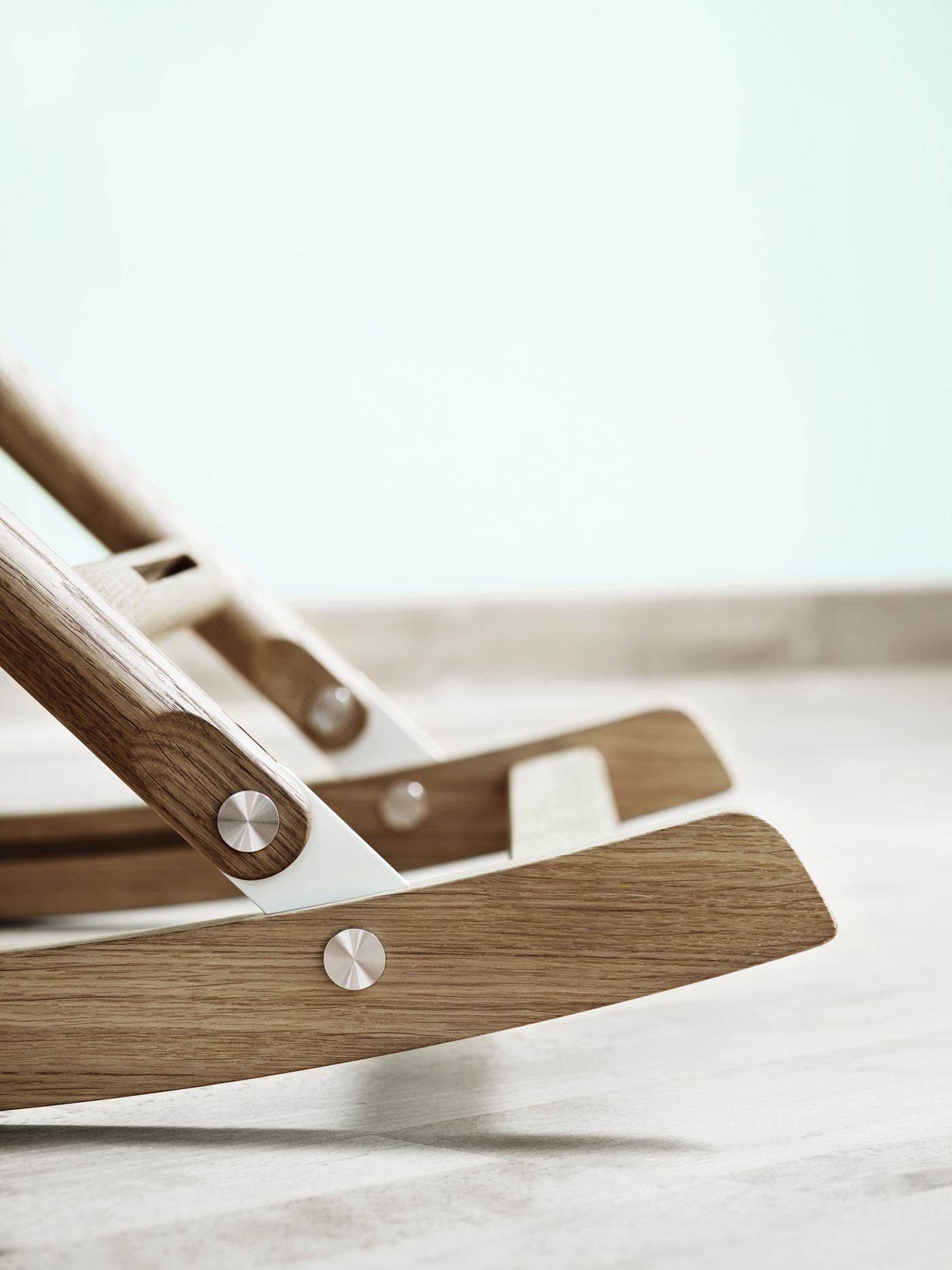 Rocking Nest Chair by Carl Hansen & Søn — a foldable rocking chair in walnut wood with a suspended canvas seat and steel cable details, shown in profile on a white background.