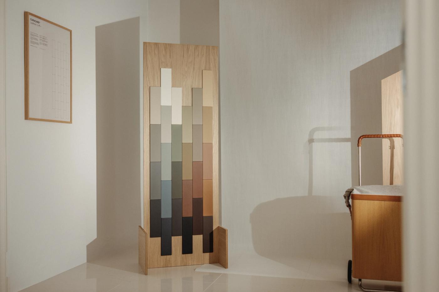 Oak sample panel displaying rows of colour and material swatches in grey, beige, rust and dark tones, beside a framed text panel on the left and a Raku trolley in oak on the right.