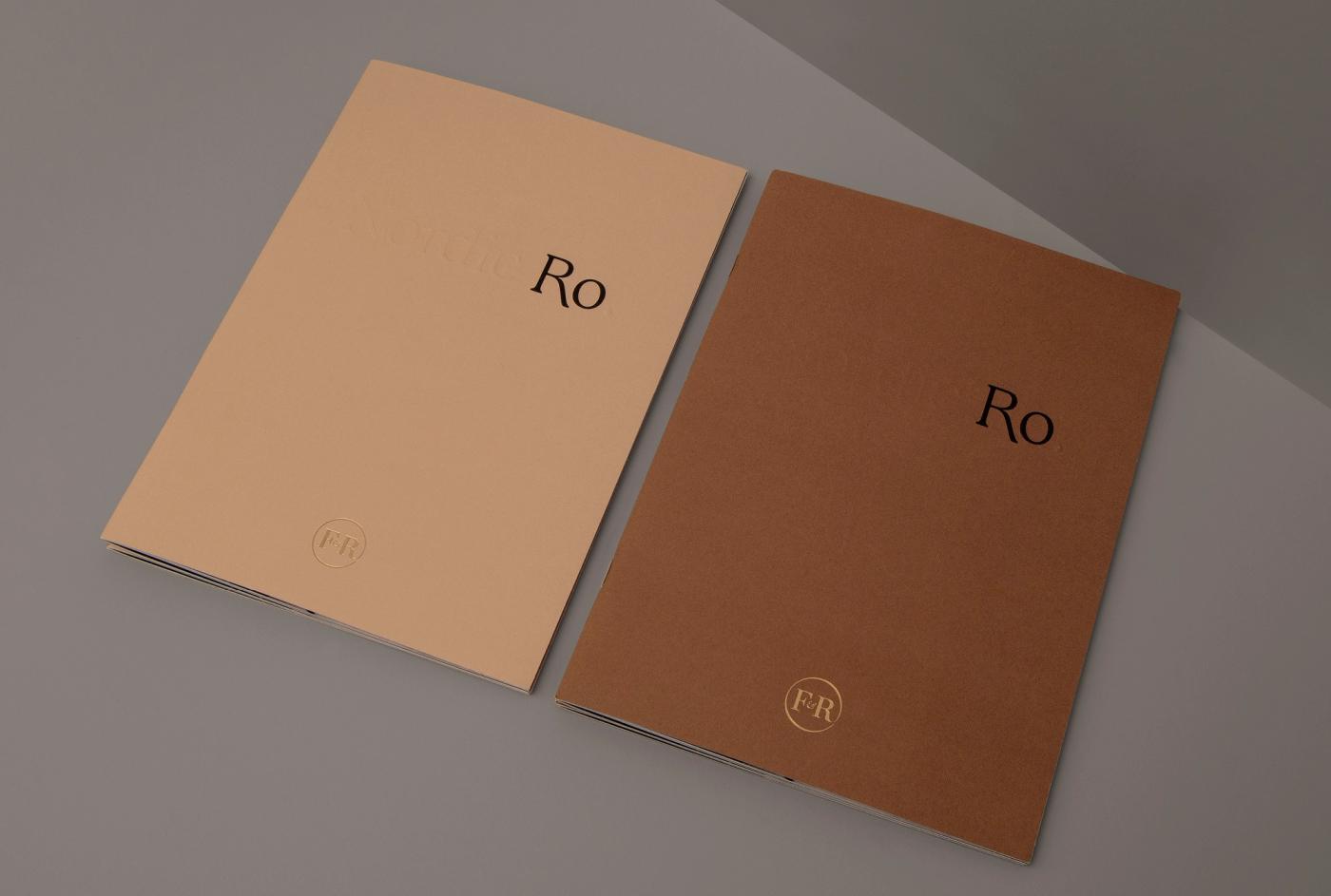 Two Ro catalogue covers side by side on a grey surface, one in peach and one in brown, each with the word "Ro" and the Fredahl Rydéns monogram.