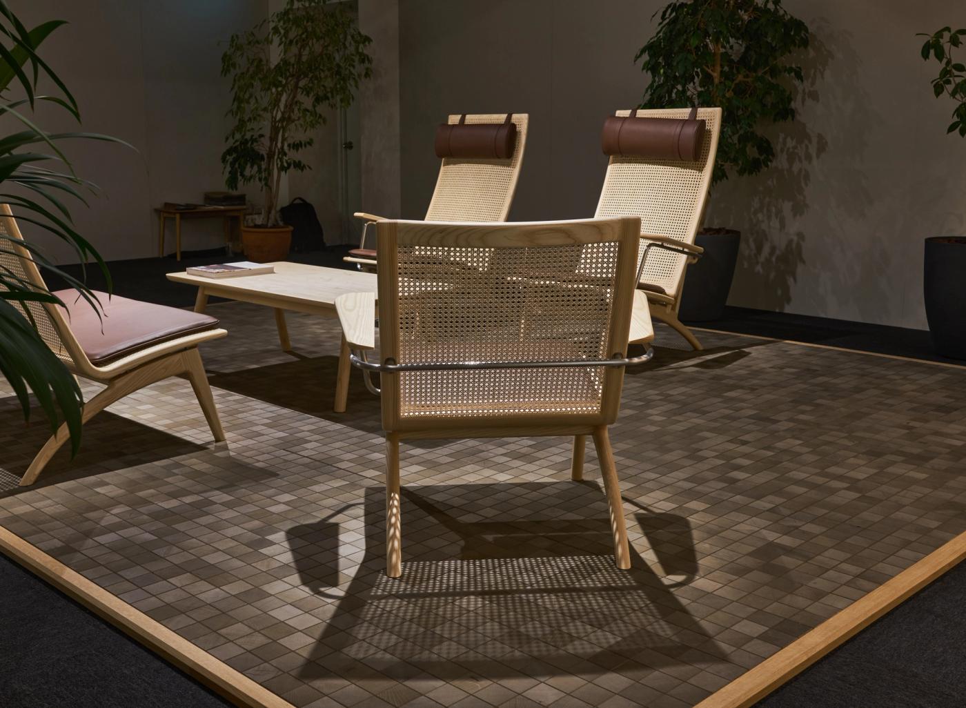 GAZE lounge chairs with woven rattan backs seen from behind, two with leather headrests and one with a brown leather seat, around a low oak table on a tiled floor.