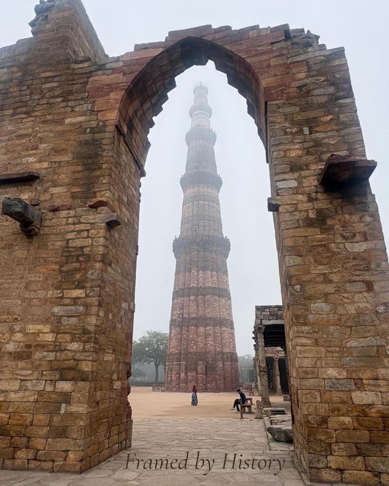 Das Qutub Minar in Delhi, gerahmt von einem alten Steinbogen