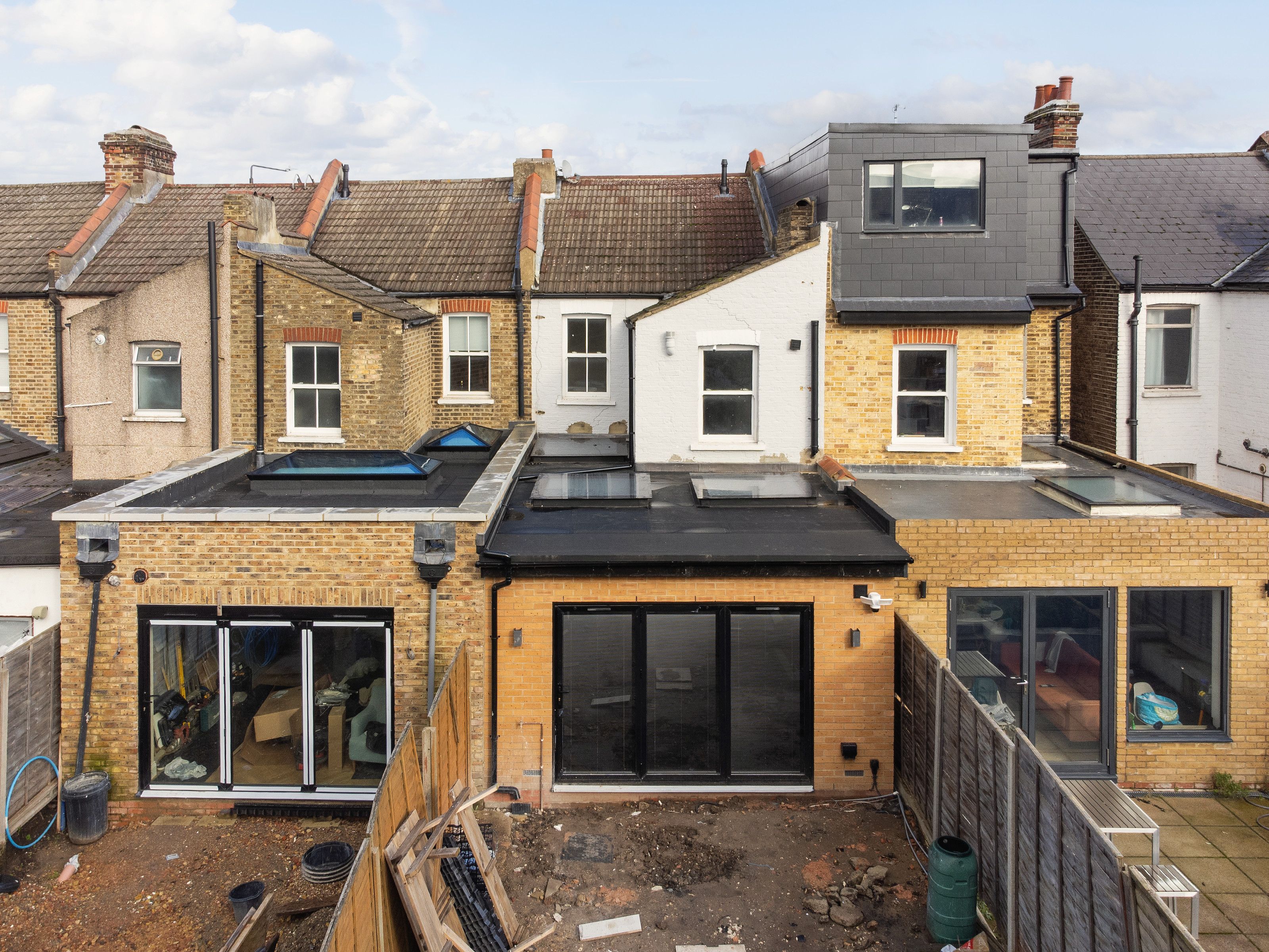 Drone view of the backs of a terrace of brick houses. The middle house has a new single-storey rear extension with a black flat roof, rooflights and wide glazed doors, and a grey dormer above