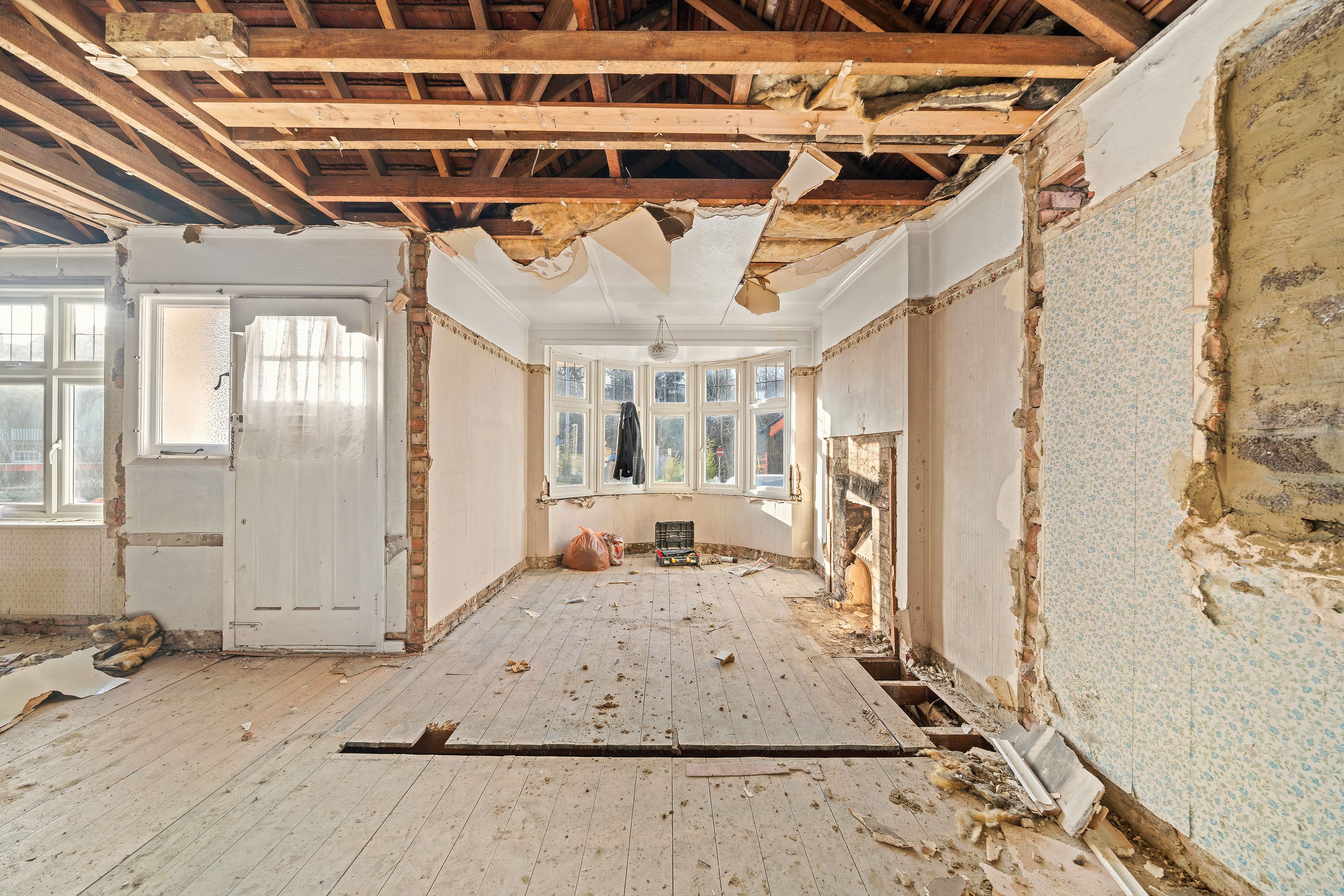 The front of the bungalow stripped back, with the ceiling partly down and the bay window beyond