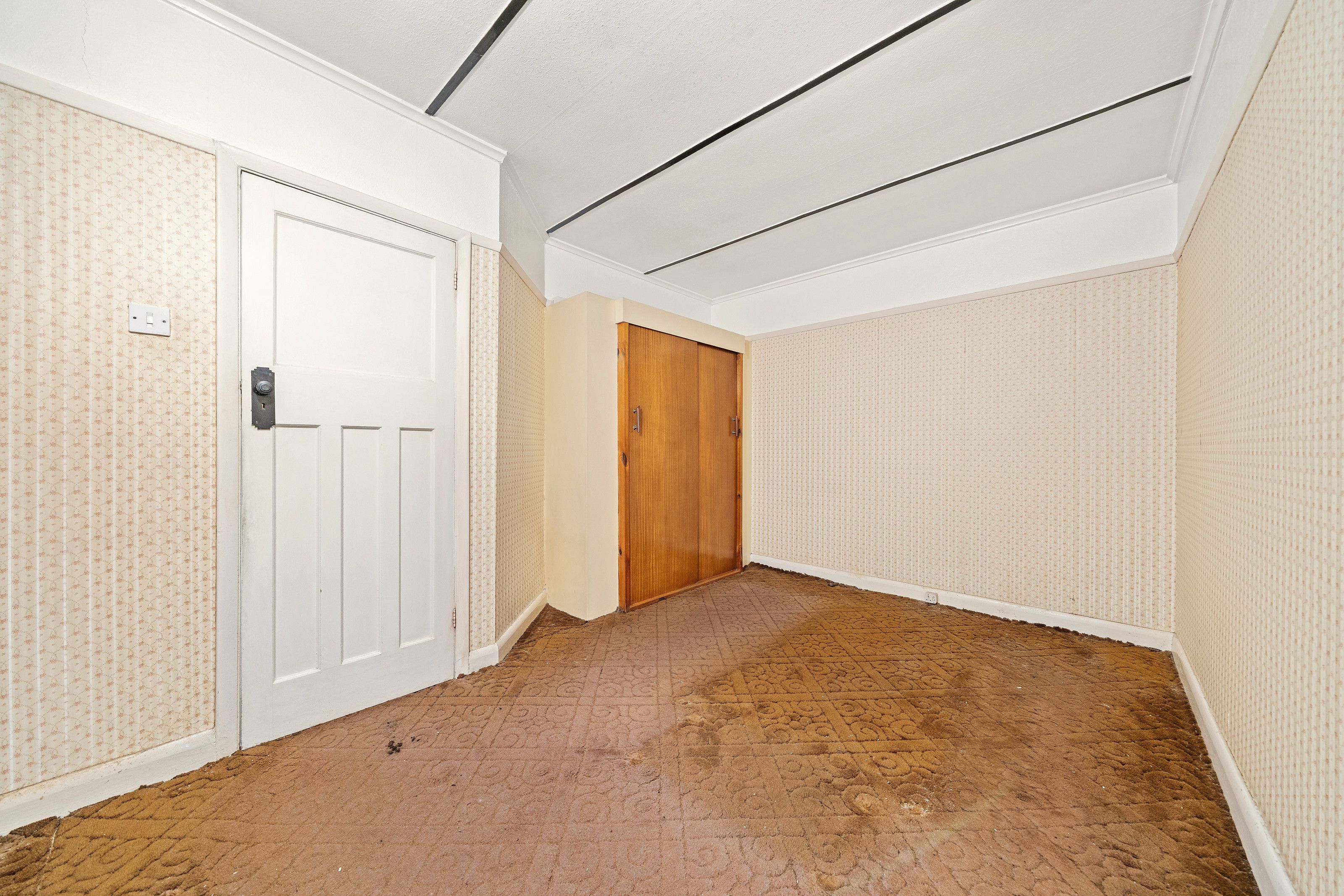 A room before the work, with old patterned carpet, textured wallpaper and a built-in cupboard