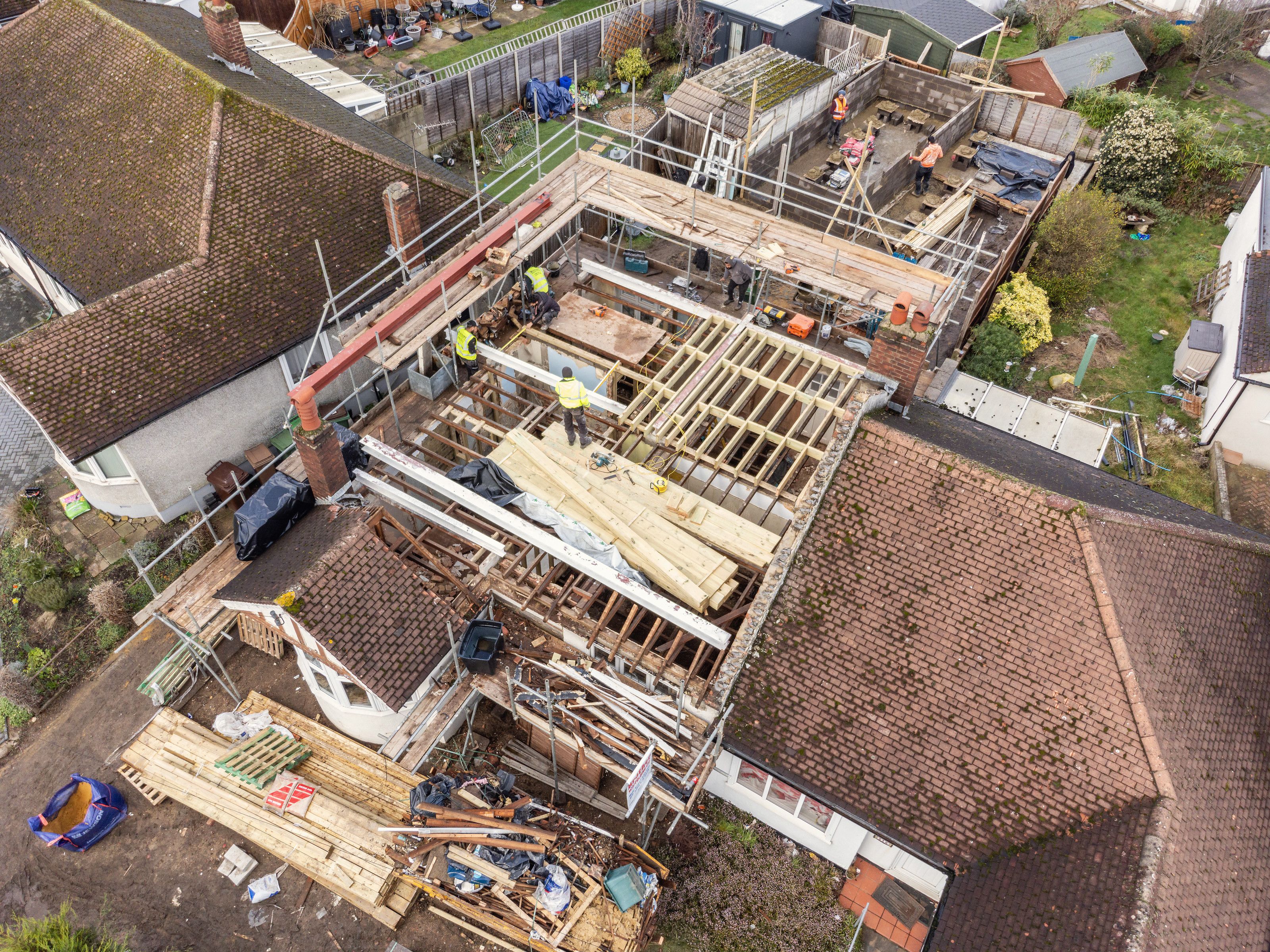 Drone view of a semi-detached bungalow with its roof opened up, new timber framing in place and builders at work