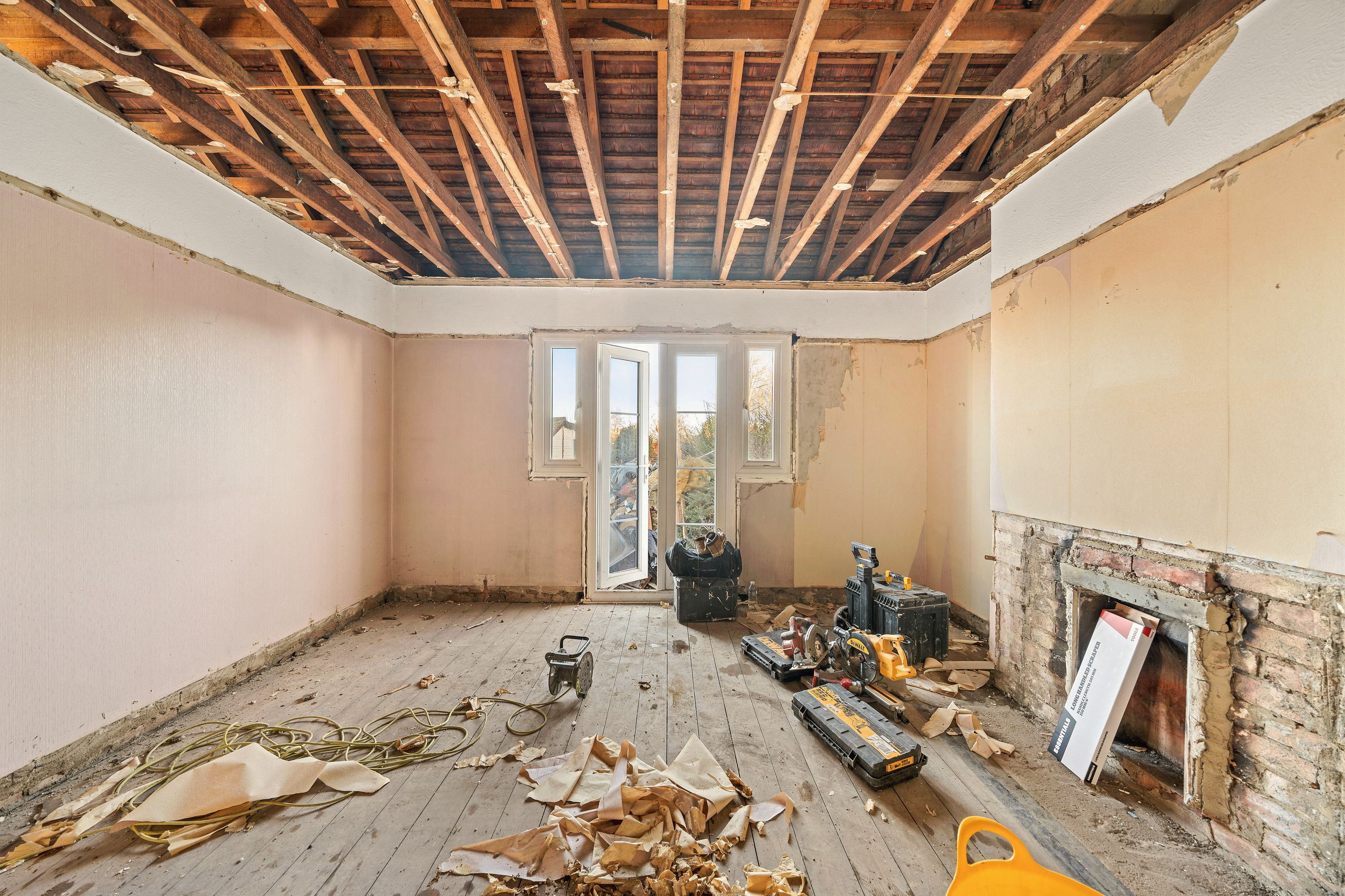 A stripped room with the ceiling joists exposed and light coming through from the rear