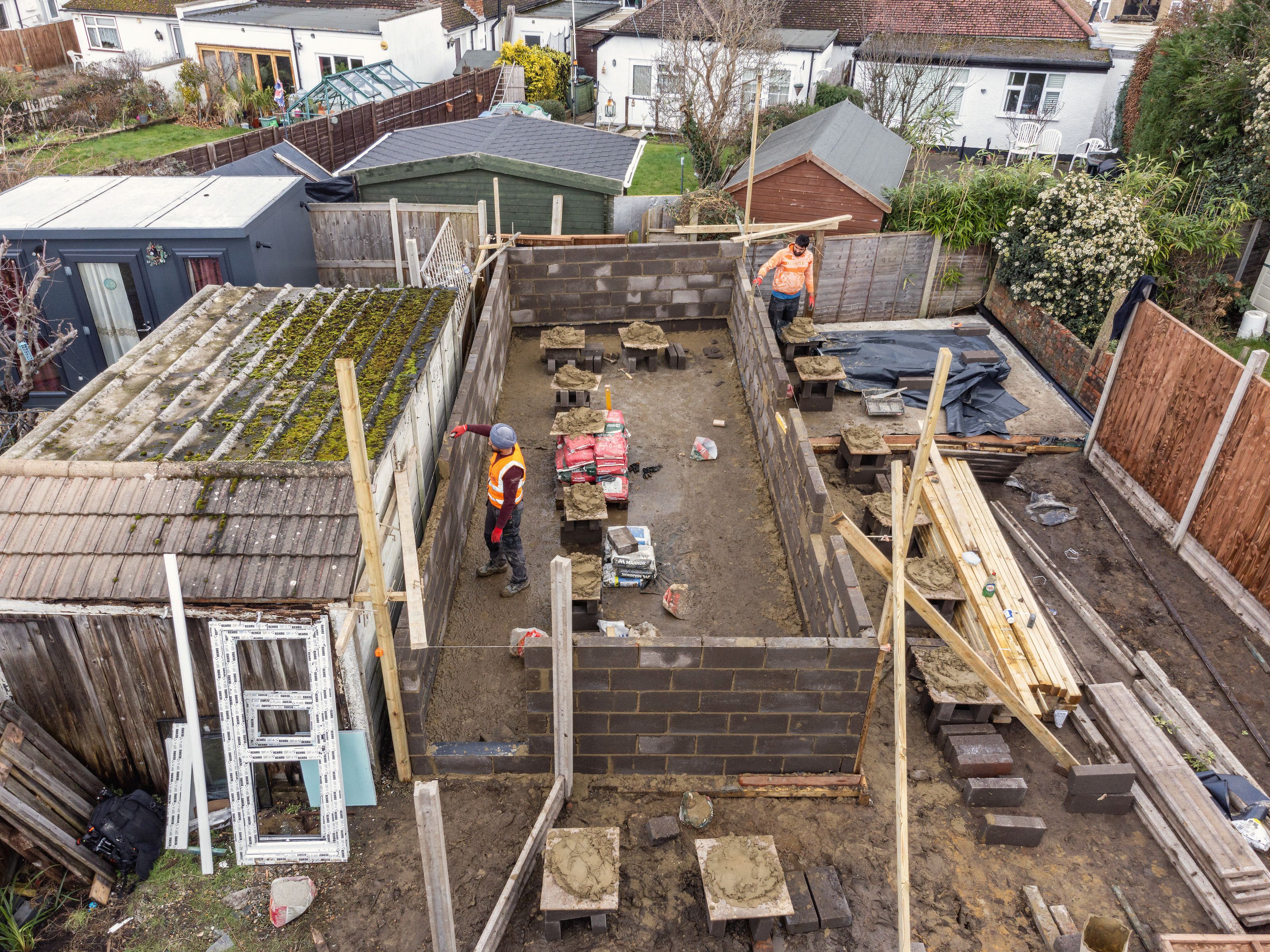 Drone view of new blockwork walls going up in the garden, with a builder at work